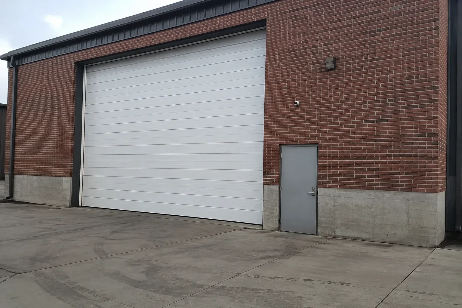 Tall closed sectional loading door beside a personnel door at a brick unit. — Commercial Sectional Door Repair, Bradford West Gwillimbury