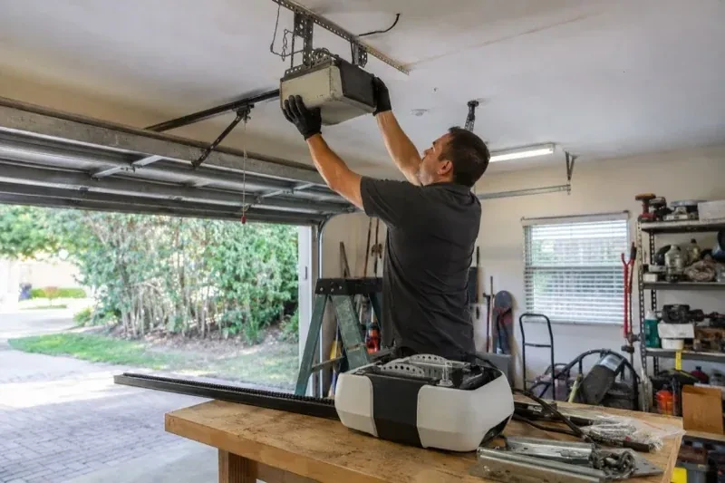 Person holding an overhead garage-door opener beside another opener and hardware on a workbench — Garage Door Opener Replacement, Bradford West Gwillimbury