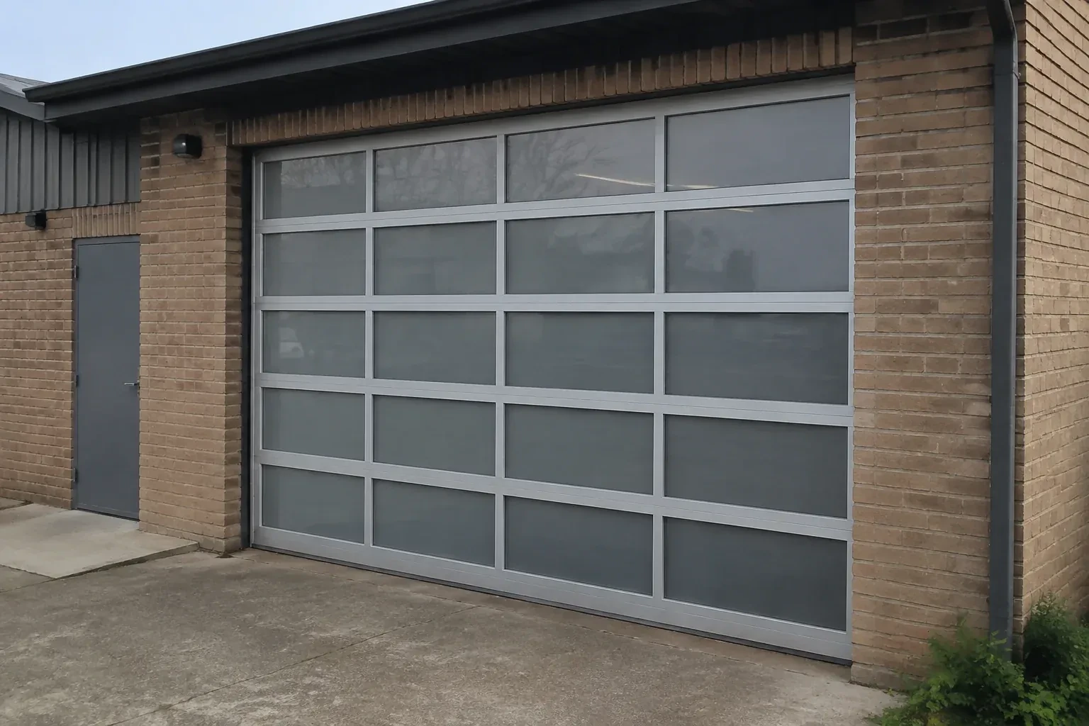 Closed glazed sectional door in a grey metal frame at a brick workshop. — Full-View Glass Garage Door Installation, Bradford West Gwillimbury